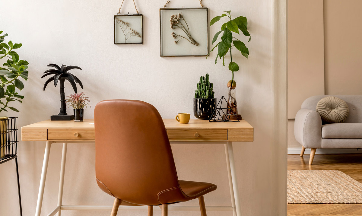 Décoration intérieure d'un espace ouvert scandinave avec des cadres photos, un bureau en bois, un canapé gris, des cactus, des livres, des accessoires de bureau et des accessoires personnels. Home staging élégant et neutre. 