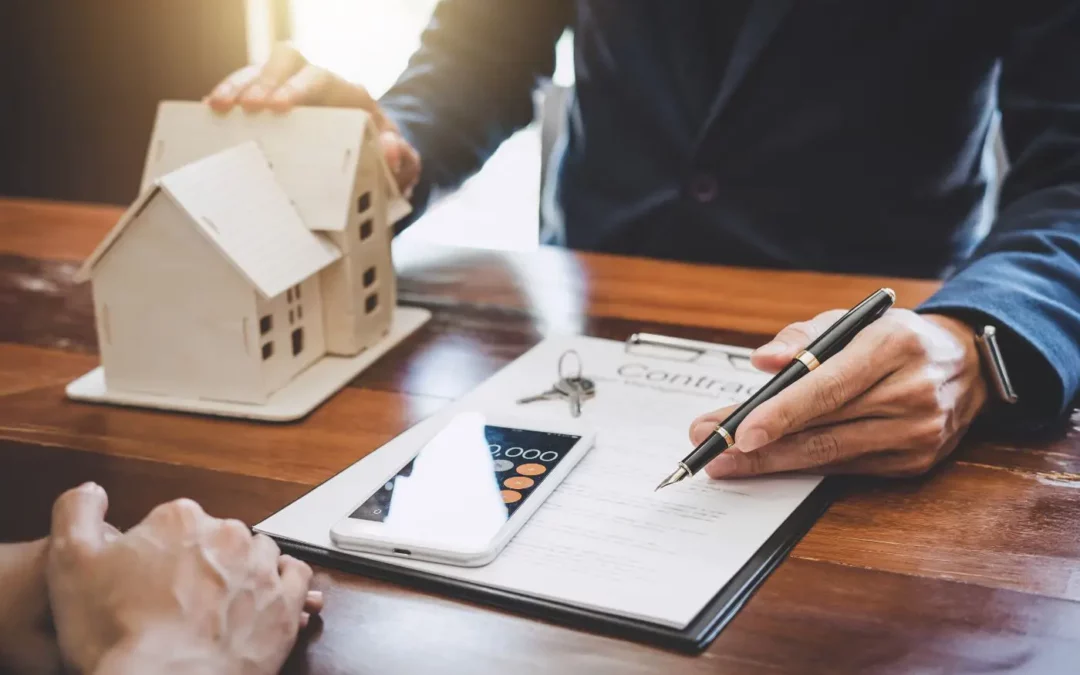 Signature d'un contrat immobilier avec une miniature de maison en bois, des clés et une calculatrice posées sur la table, symbolisant une transaction immobilière.